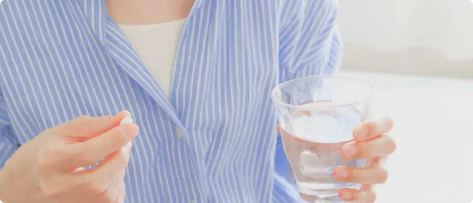 水の入ったグラスを持ちピルを服用しようとする女性