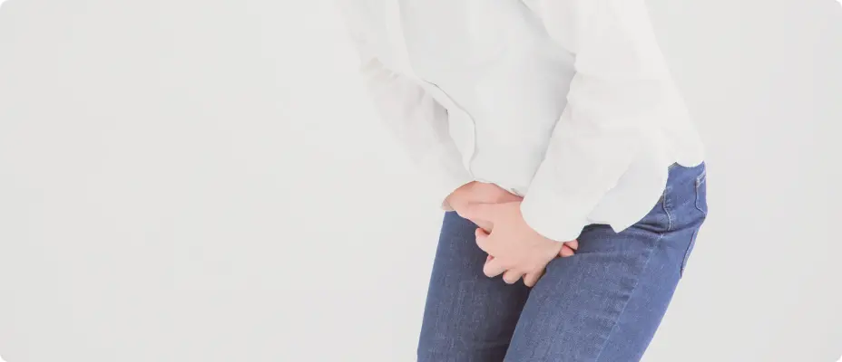 白いトップスとデニムの女性がお腹の下あたりに手を添えている写真