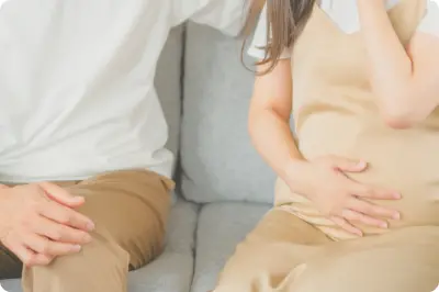ソファに座る妊婦とパートナーがお腹に手を添えている様子