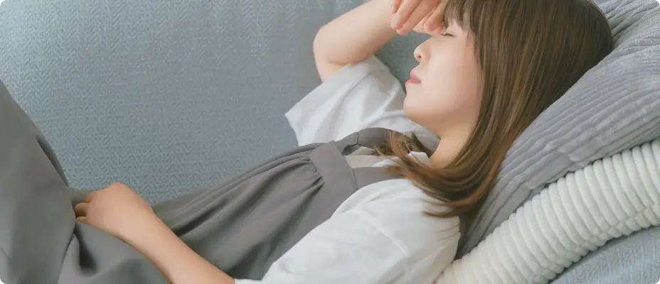 ソファで頭を押さえてつらそうにしている女性